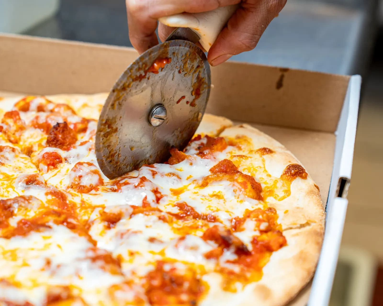 Fresh cheese pizza being sliced in the box